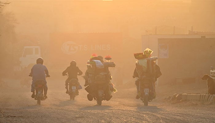 Commuters ride along a street engulfed in smog in Lahore on November 19, 2024. — AFP