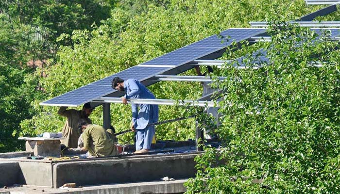 Workers busy in installation of solar panels on the top roof of a house at Bacha Khan Chowk in Peshawar on April 17, 2024. — APP