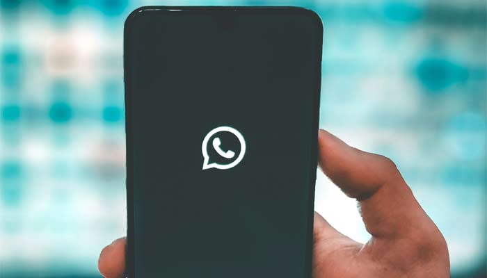 A representational image shows a person holding a phone with the WhatsApp logo displayed on the screen. — Unsplash