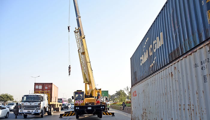 Workers busy placing heavy shipping containers near Faizabad flyover along Islamabad Highway for road block ahead of PTI protest in Islamabad — November 21, 2024. — Online