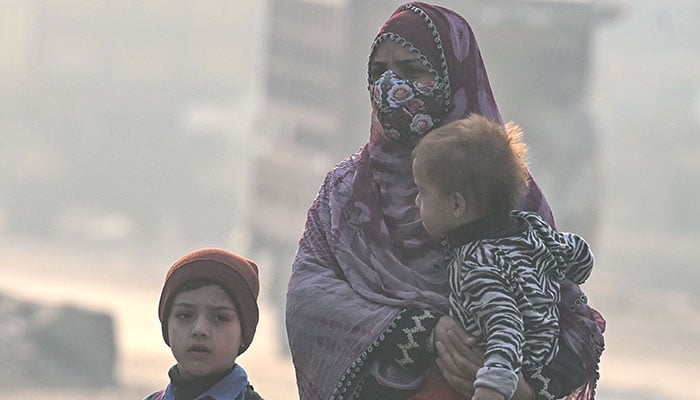 A woman with children walks on a road amid dense smog in Lahore on November 21, 2024. — AFP