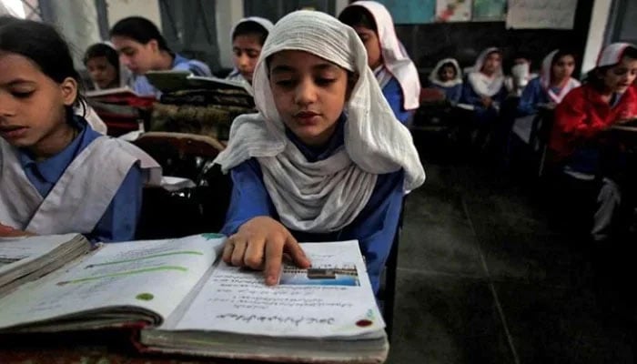 In this file photo, a girl reads a book while attending her daily class with others at a government school. — Reuters