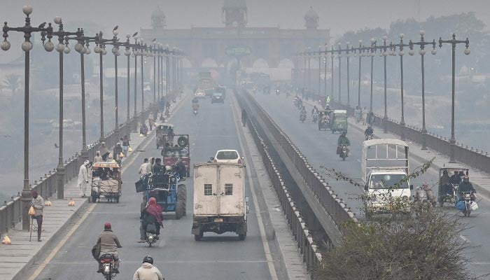 Commuters move along a road amid smoggy conditions in Lahore on November 24, 2024. — AFP