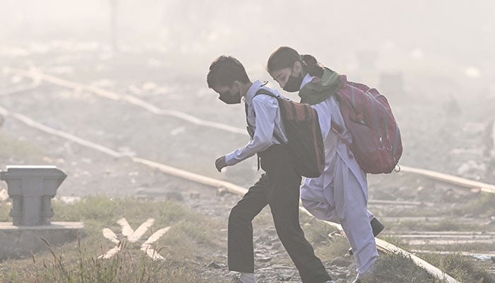 Schoolchildren wearing masks walk across a railway track amid thick smog in Lahore on November 20, 2024.