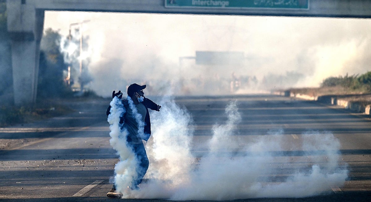 A member of jailed former prime minister Imran Khan´s Pakistan Tehreek-e-Insaf (PTI) party attempts to throw back teargas shells fired by riot policemen as they protest during a march to Islamabad in Hasan Abdal in Punjab province on November 25, 2024. —  AFP