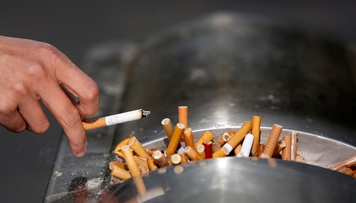 A man flicks ashes from his cigarette over a dustbin in Shanghai. — Reuters