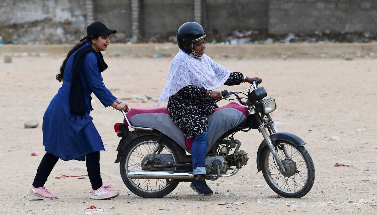 Zainab Safdar (L), an instructor with the women-only group Rowdy Riders, helps a student ride a motorbike during a riding lesson at an open ground in Karachi on March 5, 2024. — AFP