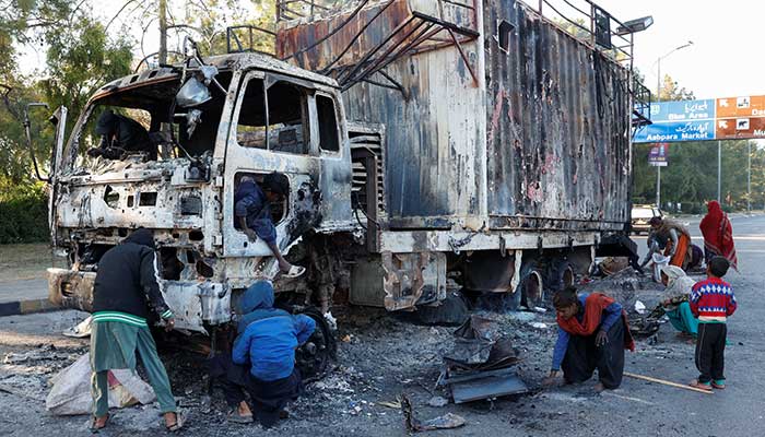 People collect recyclables from the burnt truck used by Bushra Bibi, wife of jailed PTI founder Imran Khan, after security forces launched a crackdown on PTI workers who had been protesting in Islamabad in this image released on November 27, 2024. — Reuters