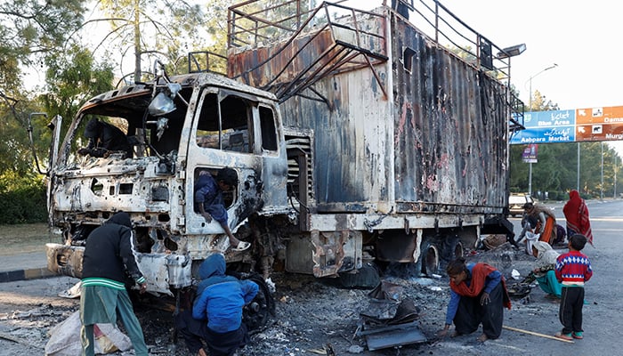 Women and children collect recyclables from the burnt truck used by Bushra Bibi, wife of PTI founder Imran Khan, in Islamabad, on November 27. — Reuters