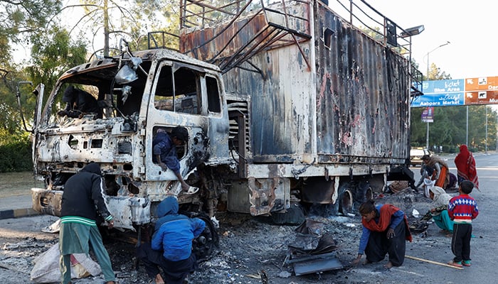 Women and children collect recyclables from the burnt truck used by Bushra Bibi, wife of jailed former PTI foinder Imran Khan, after security forces launched a raid on supporters of Khans party who had stormed the capital demanding his release on Tuesday, in Islamabad,  November 27, 2024. — Reuters