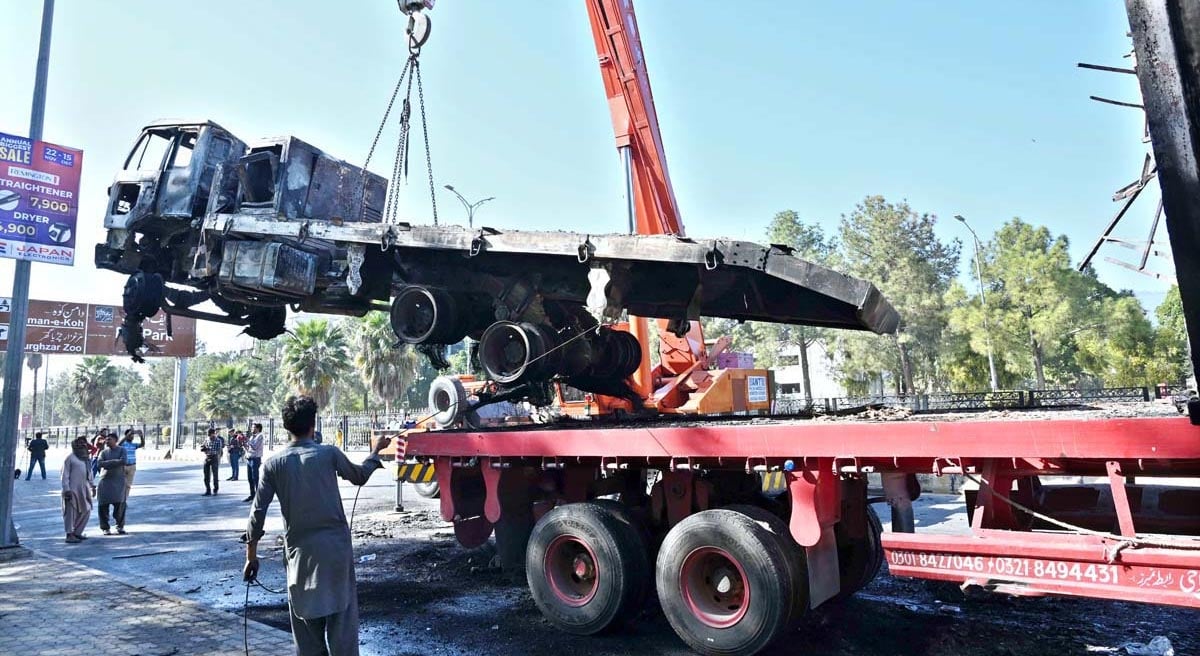 Officials busy removing the burnt container from the site at Jinnah Avenue following PTI protest in Islamabad on November 27, 2024. — APP