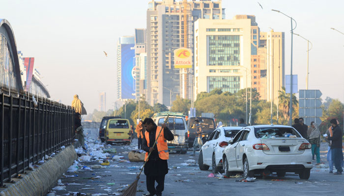 A worker clears the road, with damaged vehicles in the background, after security forces launched a raid on supporters of Pakistan Tehreek-e-Insaf who had stormed the capital demanding Imran Khans release on  November 27, 2024. — Reuters