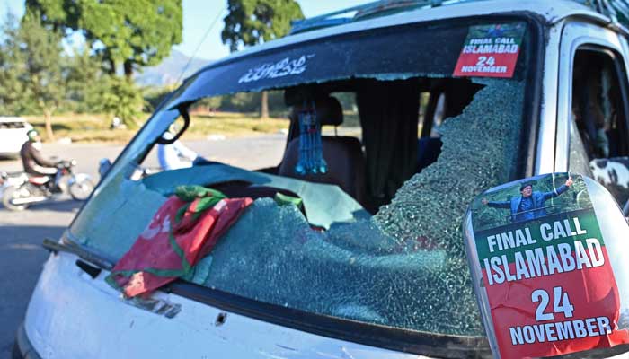 Commuters ride past a vehicle that was damaged by PTI supporters in Islamabad on November 27, 2024. — AFP