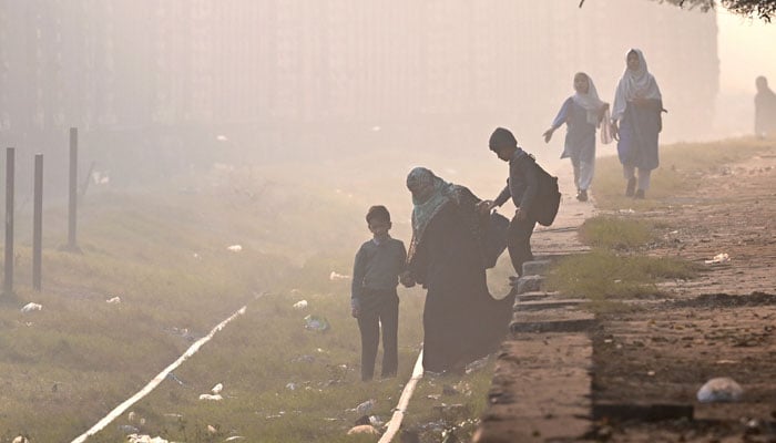 School children prepare to cross a railway track engulfed in smog in Lahore on November 27, 2024. — AFP