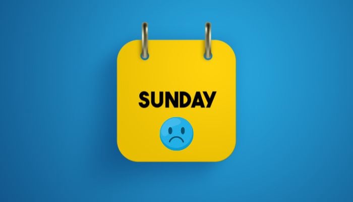 A representational image of a blue-coloured sad face emoji is pictured on a calendar page. — Canva