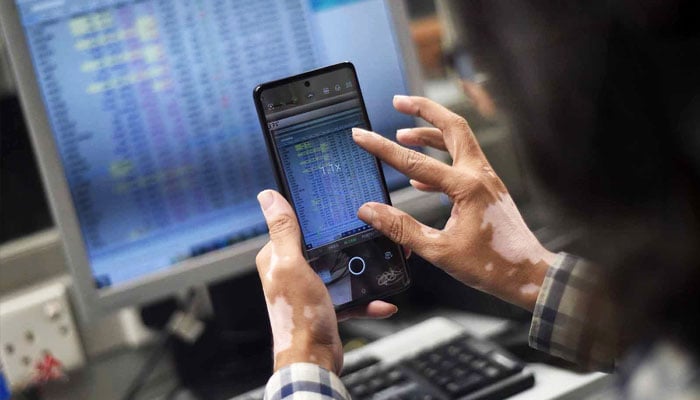 A stockbroker takes a picture with his cell phone after the Pakistan Stock Exchange made history surging past the significant 100,000-point mark, on November 28, 2024.— INP