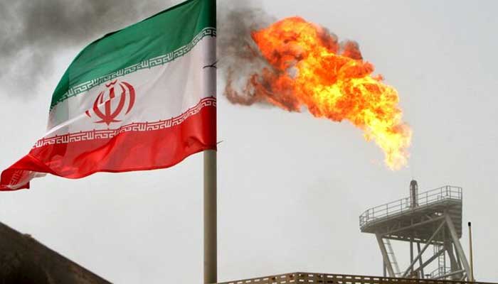 A gas flare on an oil production platform in the Soroush oil fields is seen alongside an Iranian flag in the Gulf July 25, 2005. — REUTERS