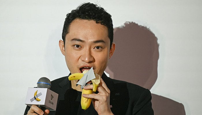 Chinese-born crypto founder Justin Sun eats a banana artwork composed of a fresh banana stuck to a wall with duct tape, in Hong Kong on November 29, 2024. — AFP