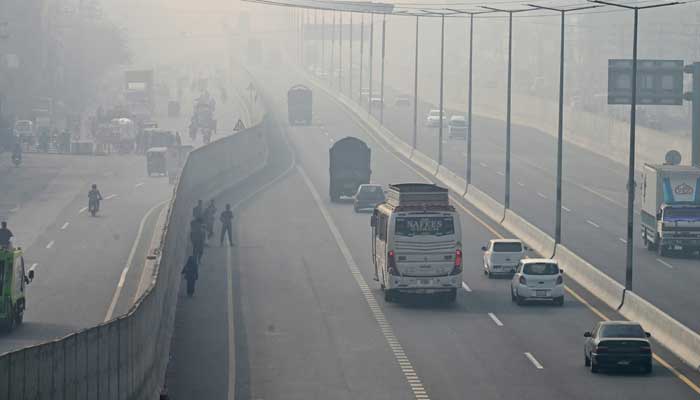 People commute along a road amid dense smog in Lahore on November 28, 2024. — AFP