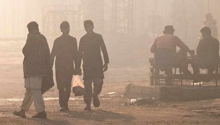 Men walk along a street engulfed in smog, in Lahore on December 2, 2024. — AFP