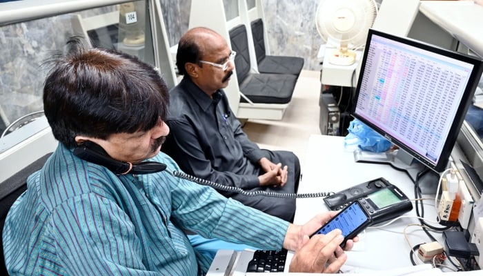 Stock brokers attend to phone calls and monitor share prices on their computers during a trading session at the PSX, on December 04, 2024. — APP