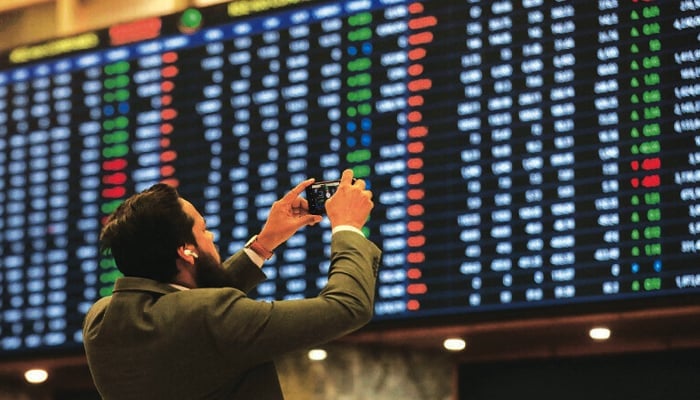 A man uses a mobile phone as he takes a photo of the electronic board displaying share prices during trading at the Pakistan Stock Exchange in Karachi. — AFP/File