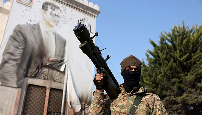 A Syrian rebel holds a weapon as he keeps position near a defaced portrait of Syrian President Bashar al-Assad, in the city of Hama after forces captured the central Syrian city, on December 6, 2024. — AFP