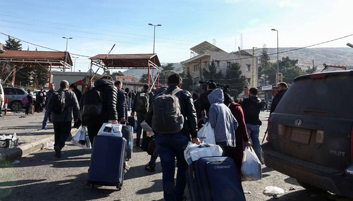 People walk with belongings as they attempt to cross into Syria, at the Masnaa border crossing between Lebanon and Syria, after Syrian rebels ousted Syrias Bashar al-Assad, December 10, 2024. — Reuters