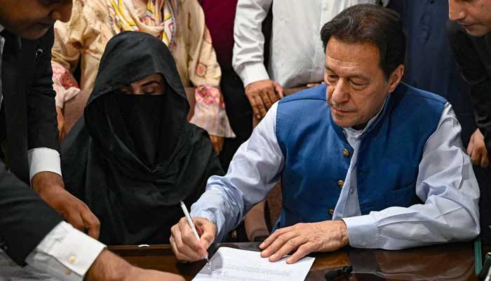 PTI founder Imran Khan pictured along with his wife Bushra Bibi, signs surety bonds for bail in various cases, at a registrars office in the Lahore High Court, in Lahore on July 17, 2023. — AFP