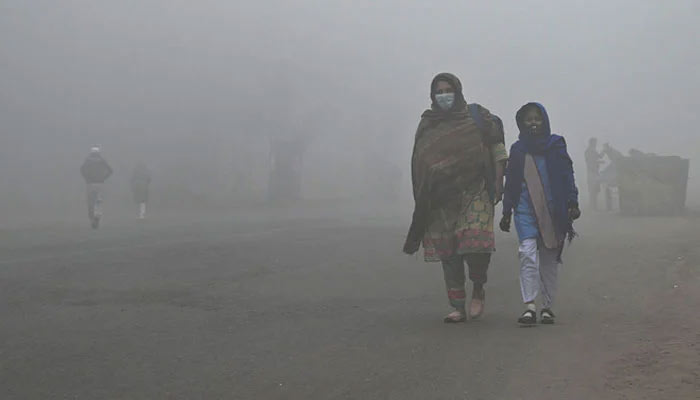 Representational image of a student walking with her mother to school in cold weather in Lahore on December 21, 2022. — AFP