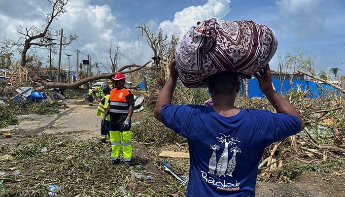 A man carries his belongings as rescue workers attempt to clear a blocked road, in the aftermath of Cyclone Chido, within Labattoir, in Mayotte, France, December 15, 2024. — Reuters