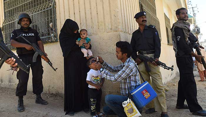 Policemen stand guard as a health worker administers polio drops to a child during a vaccination campaign against the crippling disease in Karachi. — AFP/File