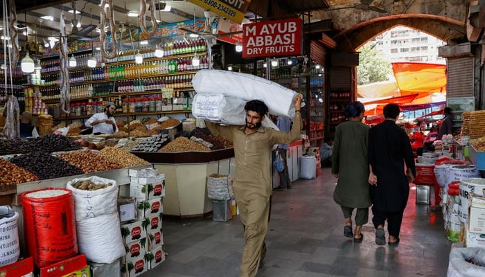 A man walks with sacks of supplies on his shoulder to deliver to a nearby shop at a market in Karachi, June 11, 2024. — Reuters