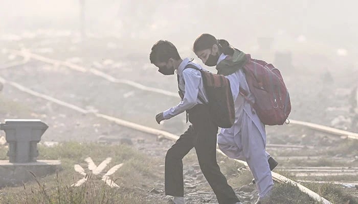 Schoolchildren wearing masks walk across a railway track amid thick smog in Lahore on November 20, 2024. —AFP