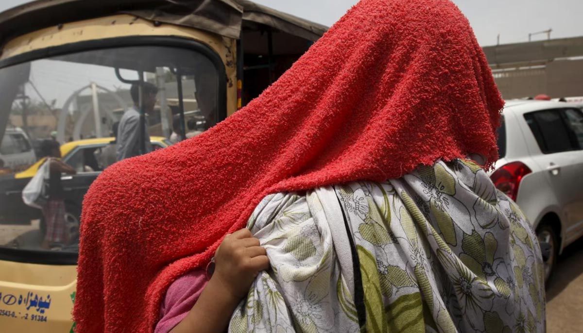 Child grabs their mothers scarf as they are both covered with a water-soaked towel, to beat the heat, in Karachi on June 24, 2015. — Reuters