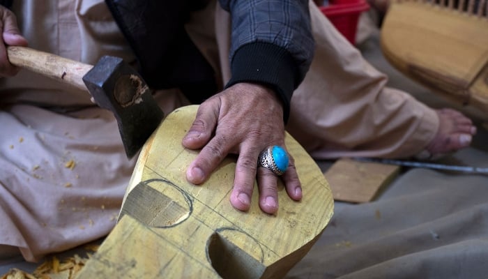 In this photograph taken on December 22, 2024, Afghan craftsman Sakhi uses a hatchet as he makes Rubab, at a workshop in Herat, Afghanistan. — AFP