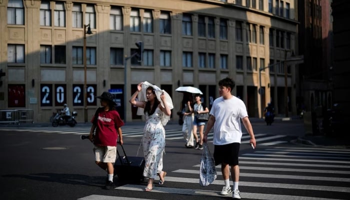 People cross a street amid an alert for heatwave in Shanghai, China August 10, 2023. — Reuters