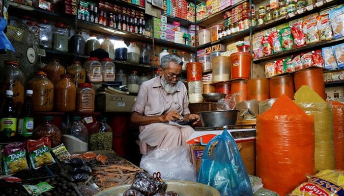 A shopkeeper uses a calculator while selling spices and grocery items along a shop in Karachi on June 11, 2021. — Reuters