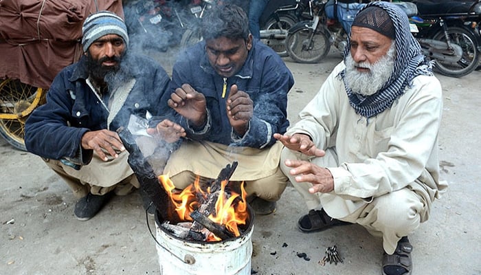 People sitting around a fire to keep them warm during chilly weather in Karachi. — APP/ File