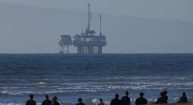 An offshore oil rig is seen as a group of people help clean the beach in Huntington Beach, California, U.S., November 14, 2024. — Reuters