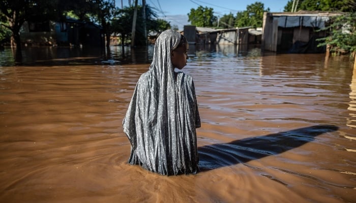 A woman wades through flood waters at an inundated residential area in Garissa, Kenya, on May 9, 2024. — AFP