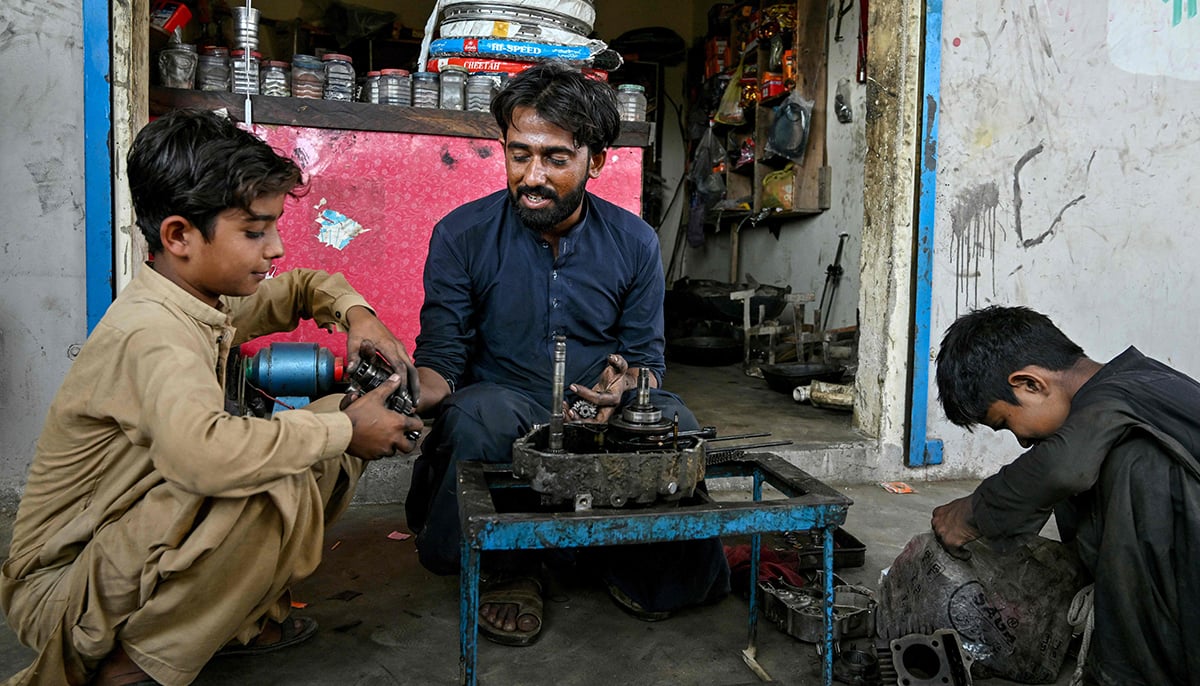 This photo taken on November 13, 2024 shows Kamran Imran (left), a 10-year-old schoolboy, working at a motorcycle workshop after finishing school in Abdullah Goth village on the outskirts of Karachi. — AFP