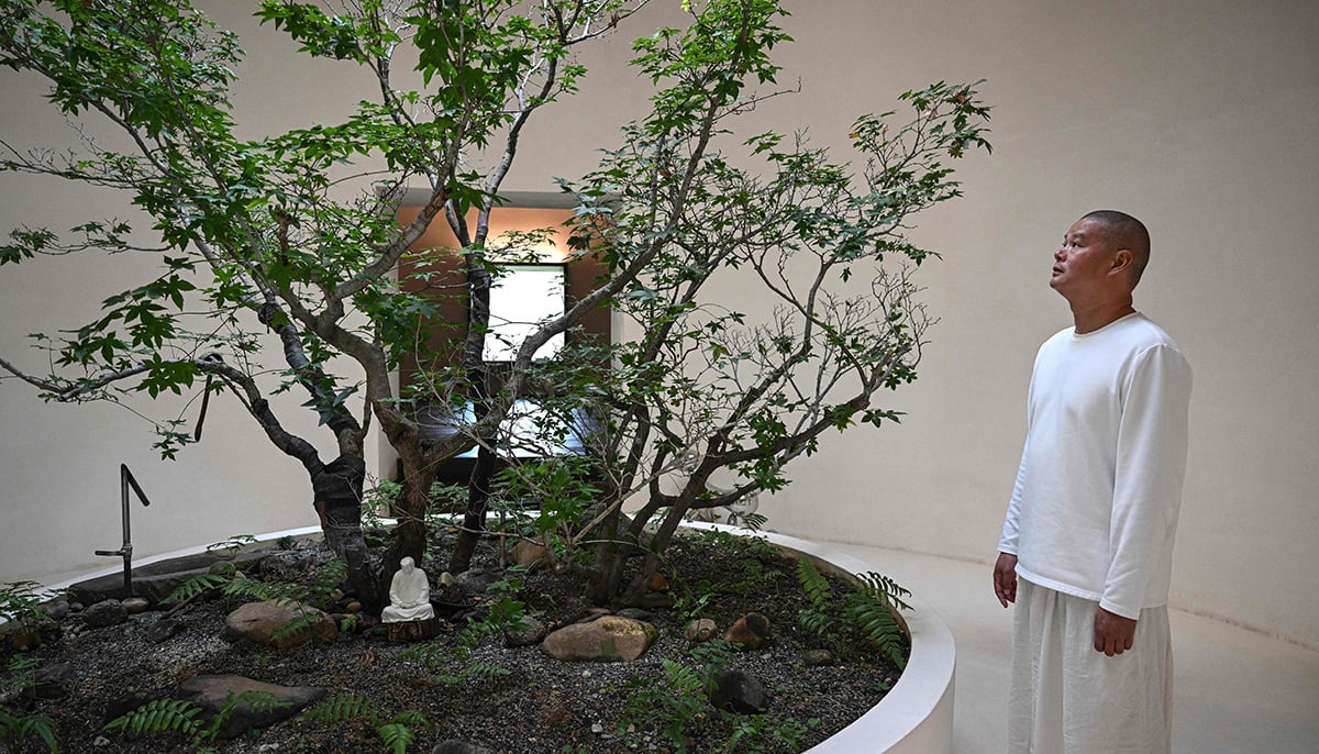 This photo taken on December 9, 2024 shows artist Hong Jinshi standing next to a tree with a small sculpture of US president-elect Donald Trump in a pose evoking the Buddha at his workshop in Xiamen, in southeastern Chinas Fujian province. — AFP