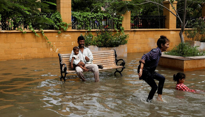 A man with a baby sits on a bench while children play amid flooded street during the monsoon season in Karachi, on July 11, 2022. — Reuters