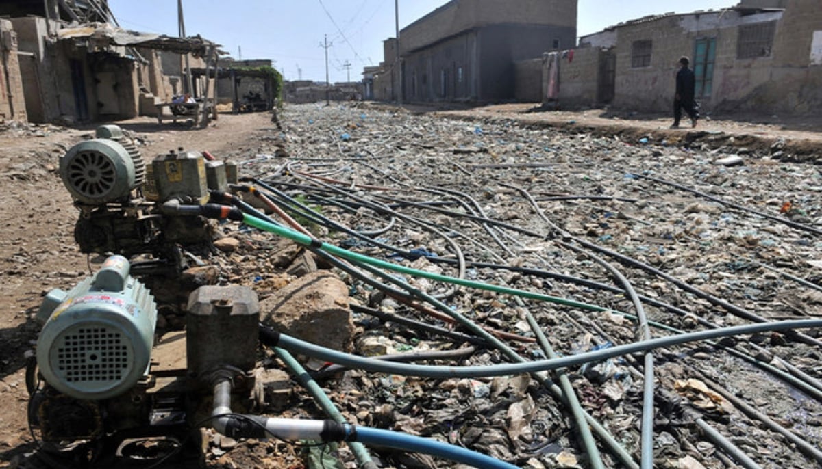 A Pakistani resident walks past pumps affixed to a network of pipes placed above garbage and drains to get water supplies in a slum area of Karachi on April 22, 2010. — AFP