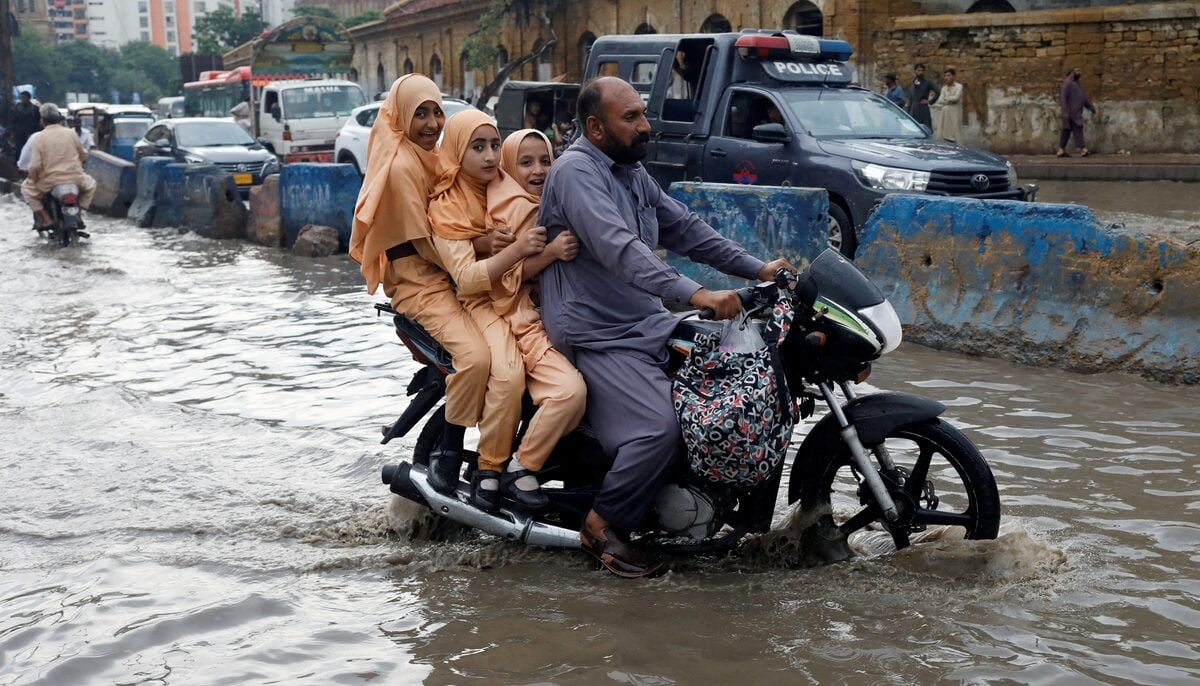 A man and students ride on a motorcycle on a flooded road, following rains during the monsoon season in Karachi on August 10, 2022. — AFP