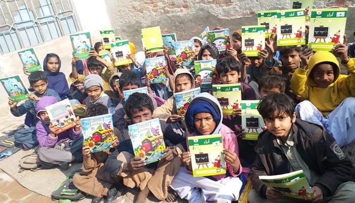 Students display their textbooks during an open-air classroom session at a non-formal school.— Literacy.punjab.gov.pk