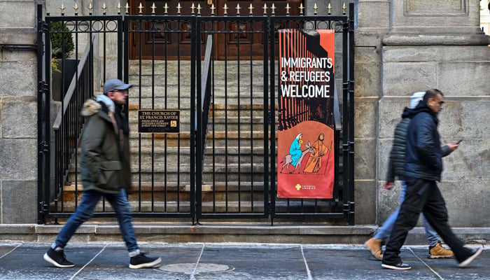 People walk past a church displaying an Immigrants & Refugees Welcome sign in New York on January 24, 2025. — AFP