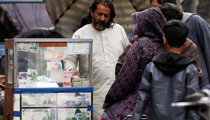 A currency broker stands near his stand, which is decorated with photos of currency tickets, while dealing with customers, along a road in Karachi, Pakistan, January 27, 2023.— Reuters