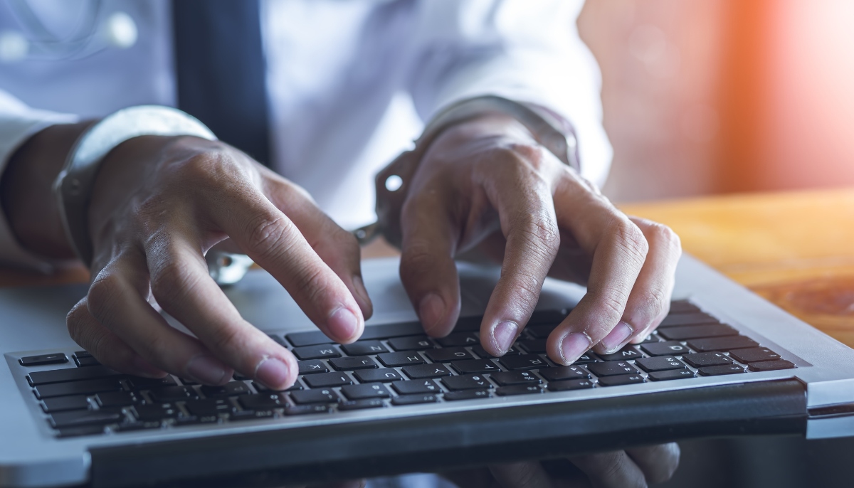 A representational image showing a person typing on a keyboard with their hands cuffed. — Canva